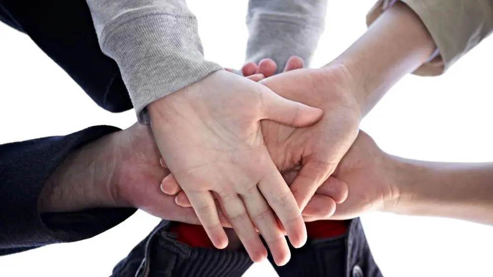 A close up image of a group of people putting their hands together