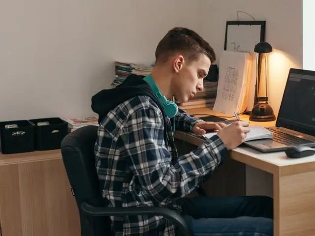 Teenager writing notes while on laptop