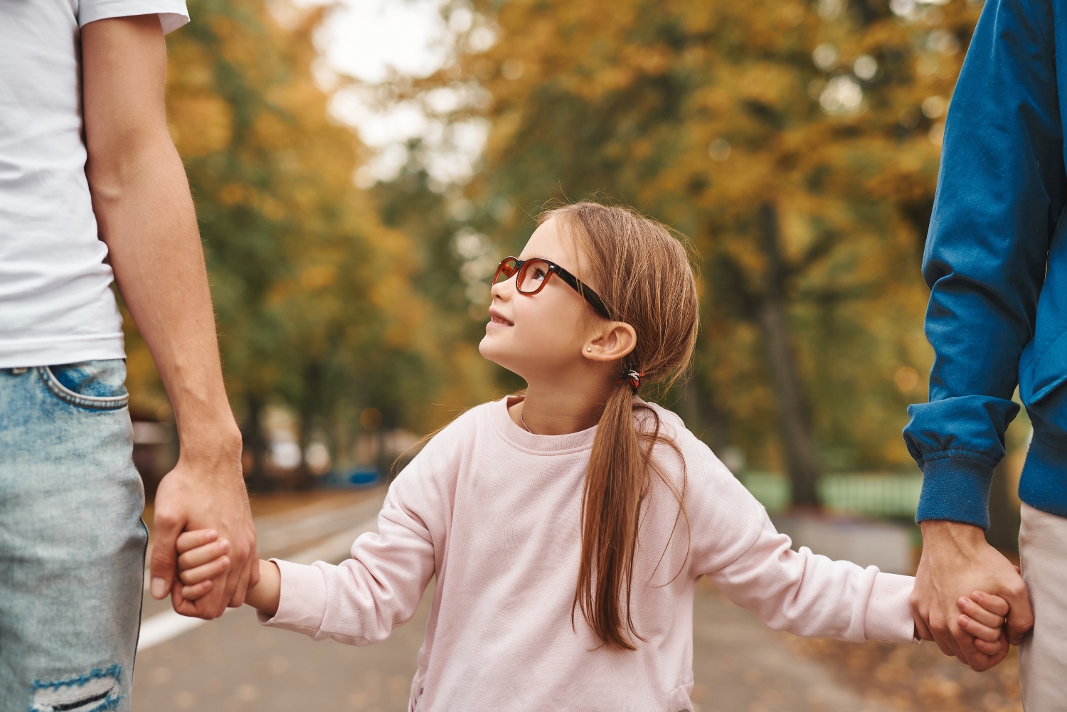 young-girl-with-glasses-looking-smiling-at-father-holding-hands-parents
