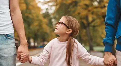 young-girl-with-glasses-looking-smiling-at-father-holding-hands-parents